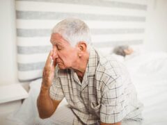 Older man, who can’t sleep at night, sitting on bed while spouse sleeps