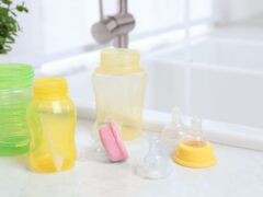Baby bottles and nipples sit on a white countertop beside the kitchen sink after being washed.